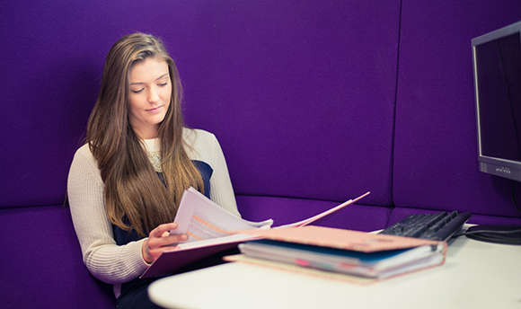 A Queen Margaret University student reading over their work against a purple wall