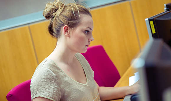 A Queen Margaret University student working alone at their computer desk, Edinburgh