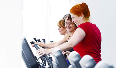Two women smiling and looking at the screen of the exercise machine one of them is using