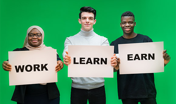 Three Queen Margaret University students holding signs with the words "Work", "Learn" and "Earn"